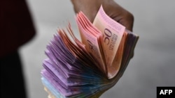 Un hombre sostiene un mazo de bolívares en una calle de Caracas.